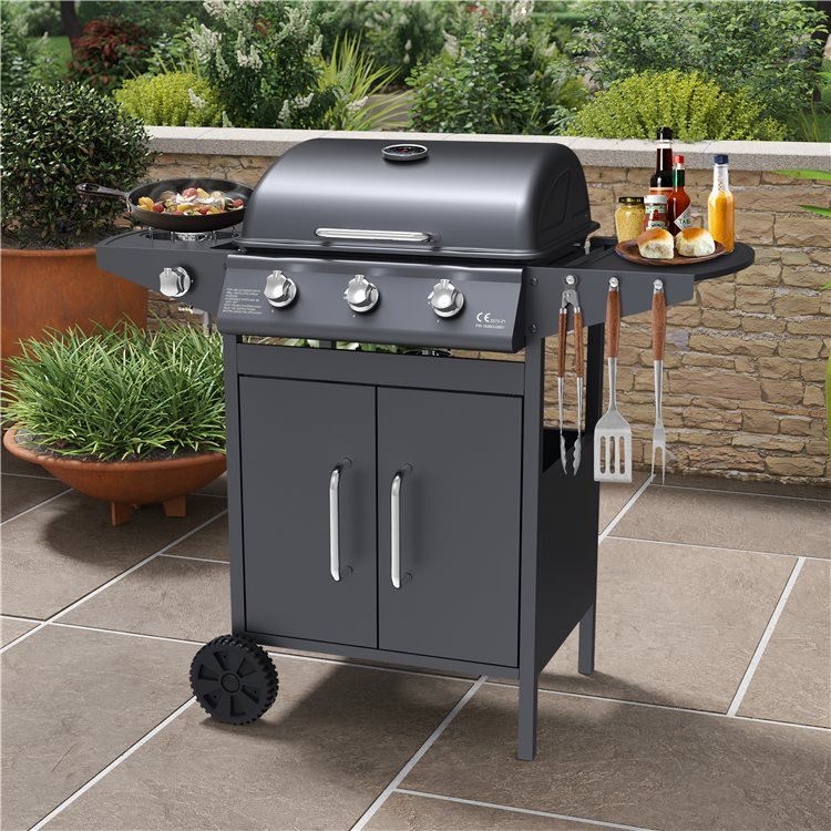 Matrix 3 Burner BBQ with lid and doors closed, equipped with sauce bottle and cooking utensils, in green a patio garden.